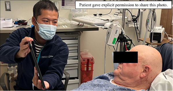 A physician holds up a table to display a video to patient lying in a hospital bed. Text on the image reads: Patient gave explicit permission to share this photo.