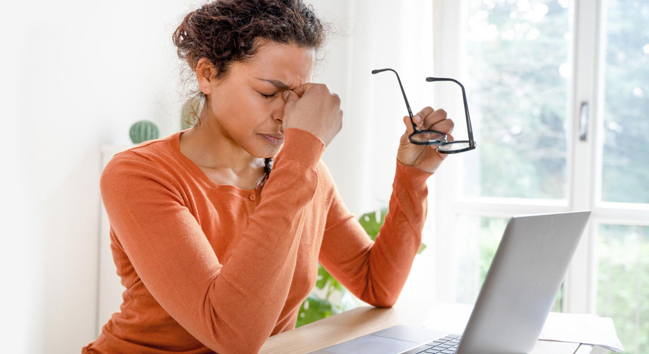 A woman pinches the bridge of her nose in front of her laptop, which can be a seizure trigger