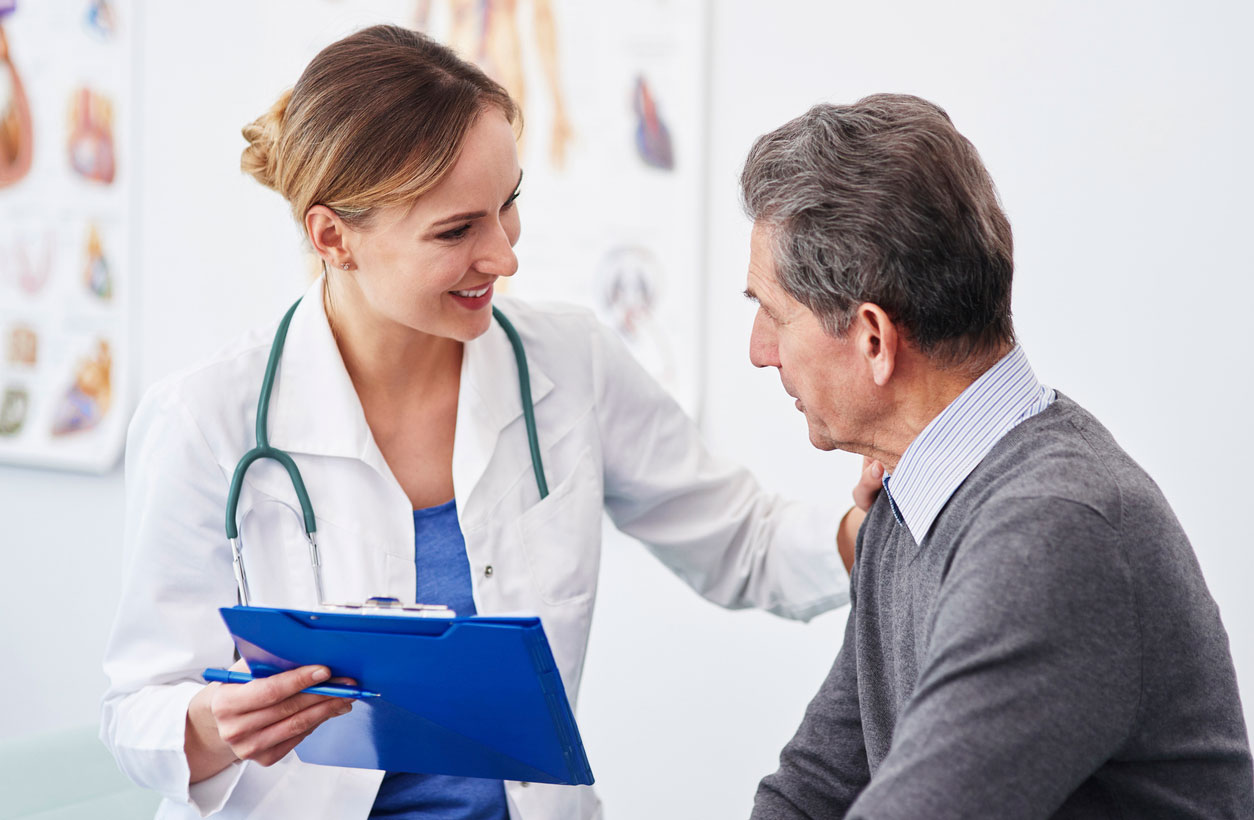 A female doctor talks supportively with an older male patient.