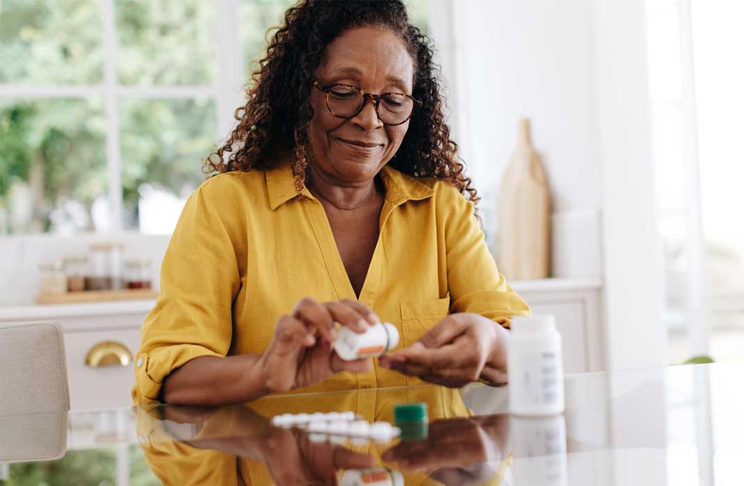 An older woman takes a pill at her kitchen table.