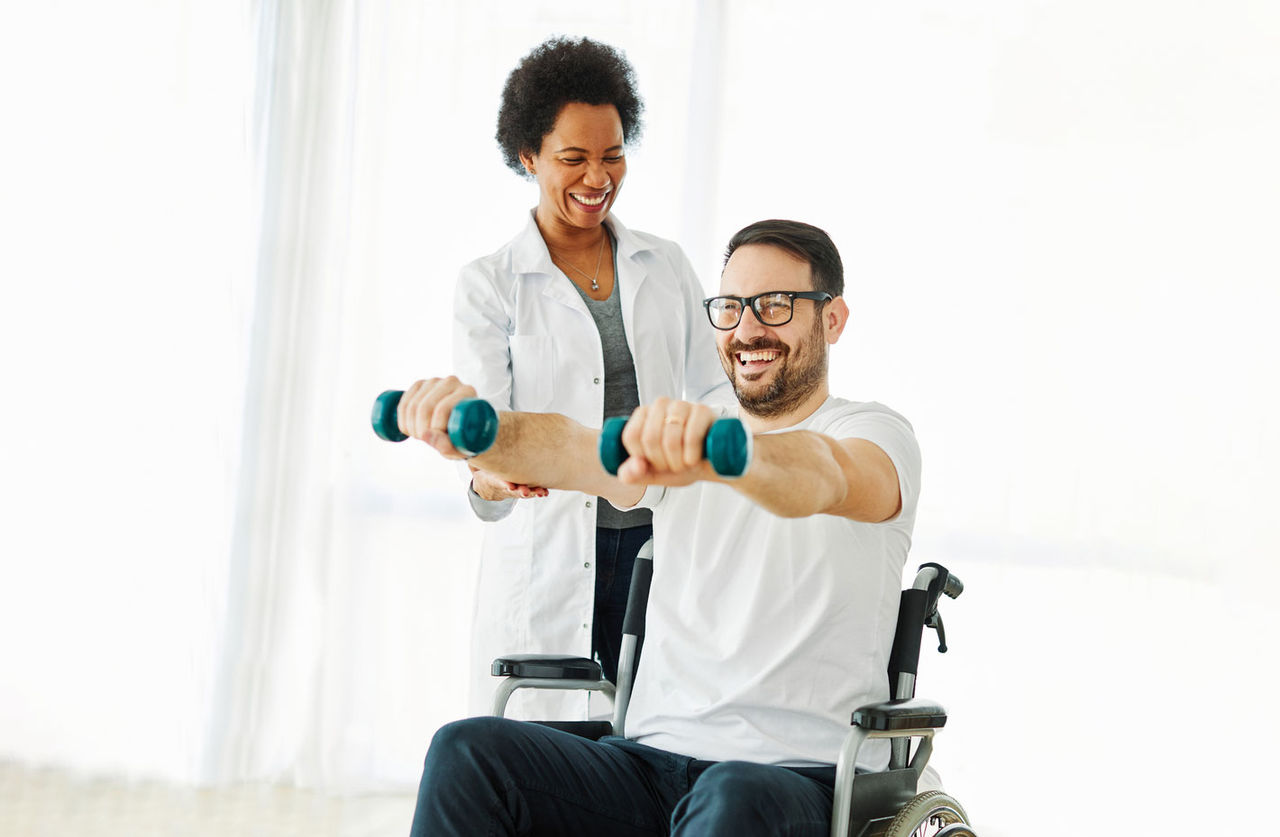 A man in a wheelchair does exercises with hand weights, guided by a physical therapist.