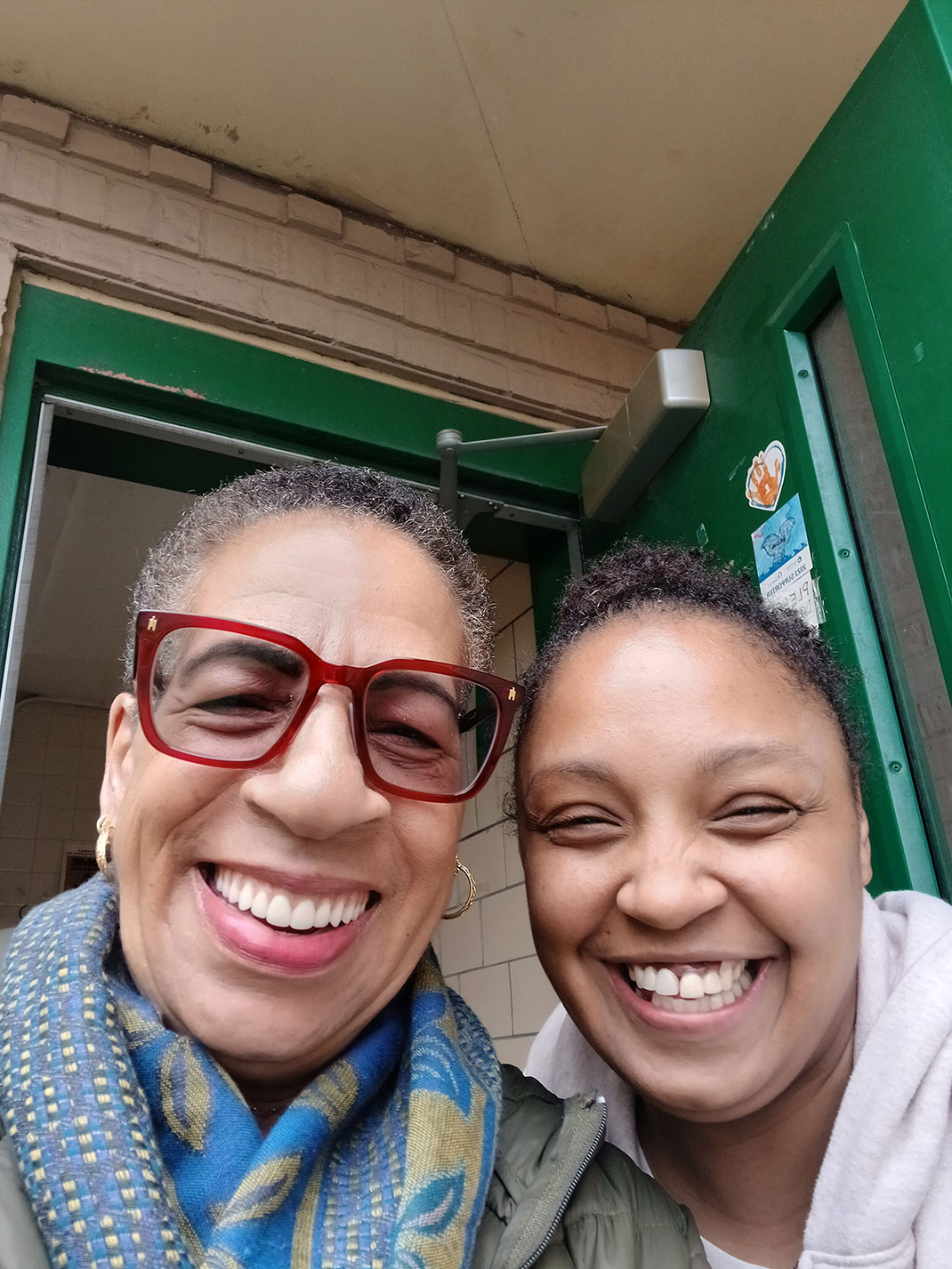 Two women take a selfie in the entryway to a building.