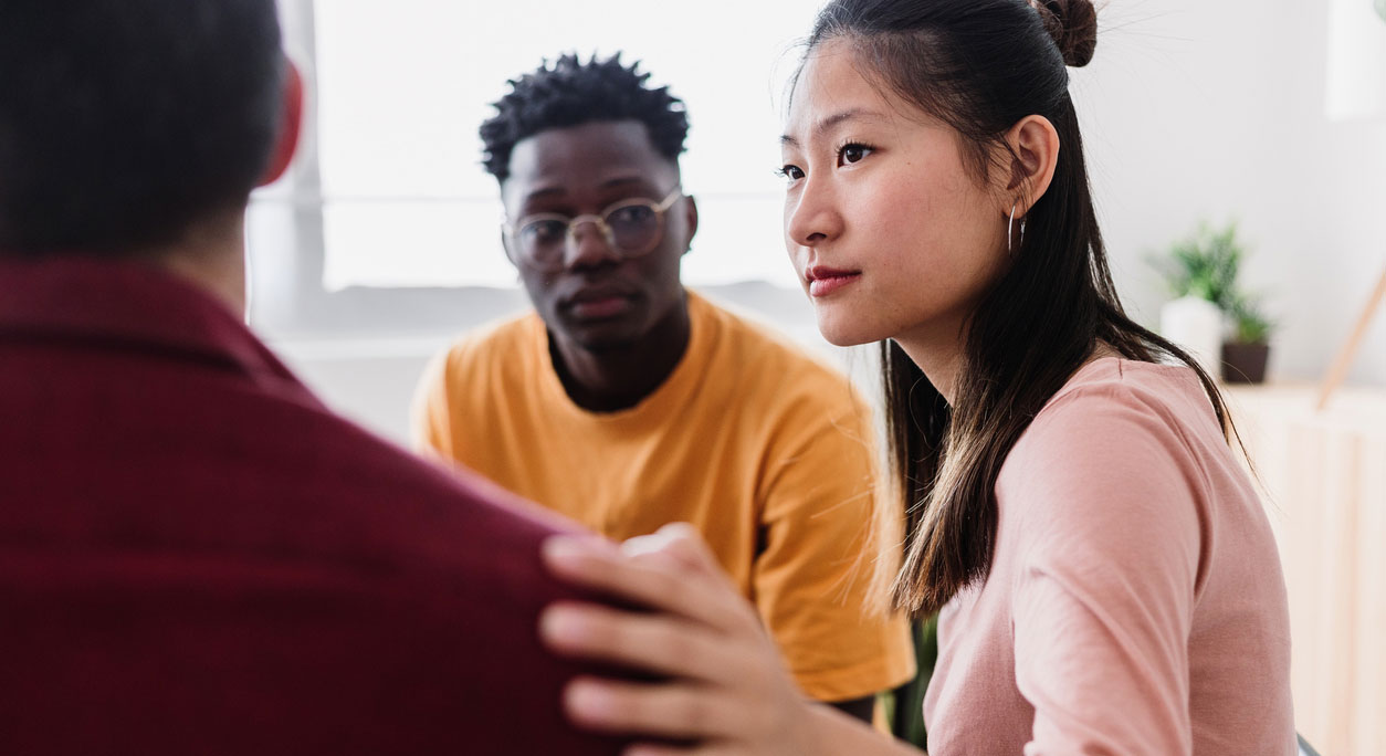A woman put a comforting hand on a man's shoulder during a group therapy session.