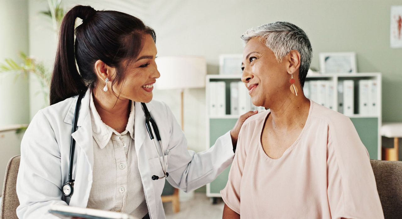 A woman of color neurologist wearing a white coat comforting a new patient, an older woman of color with short gray hair