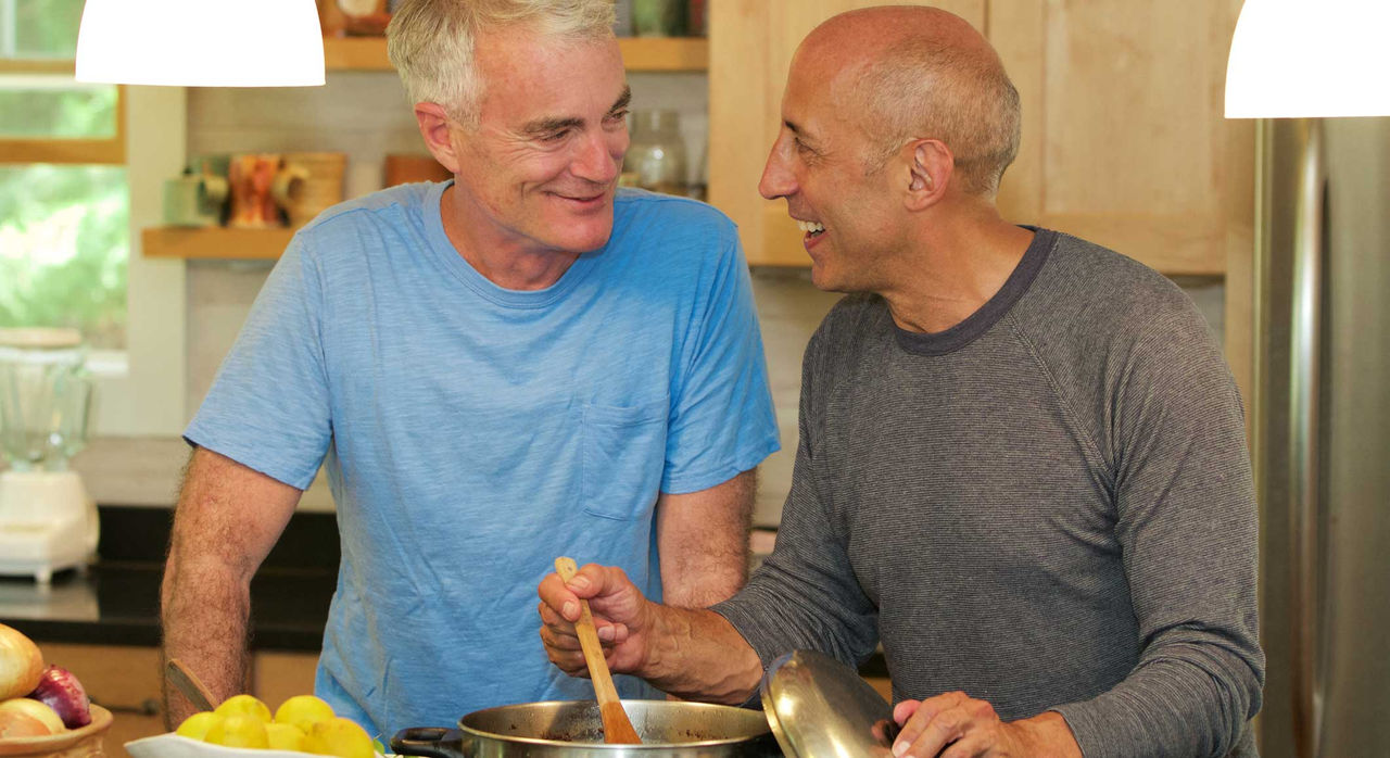 Two men sharing a moment as they stir a pot on the stove.