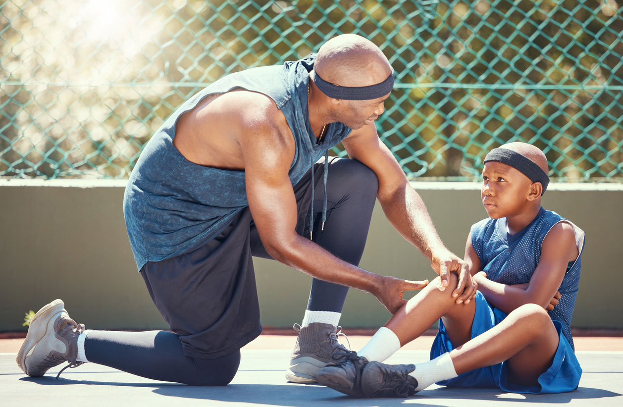 A boy sits on a basketball court as an adult checks his leg for an injury.