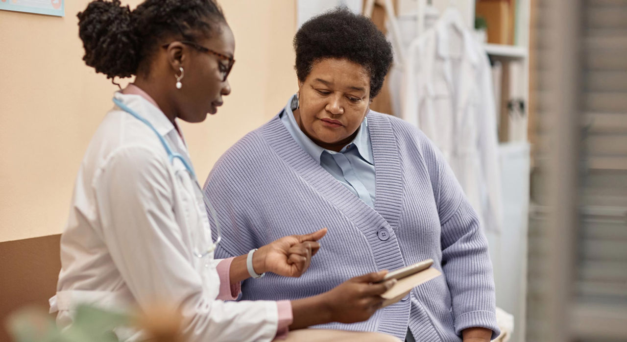 An older African American patient meets with her doctor, who shares information on a tablet.