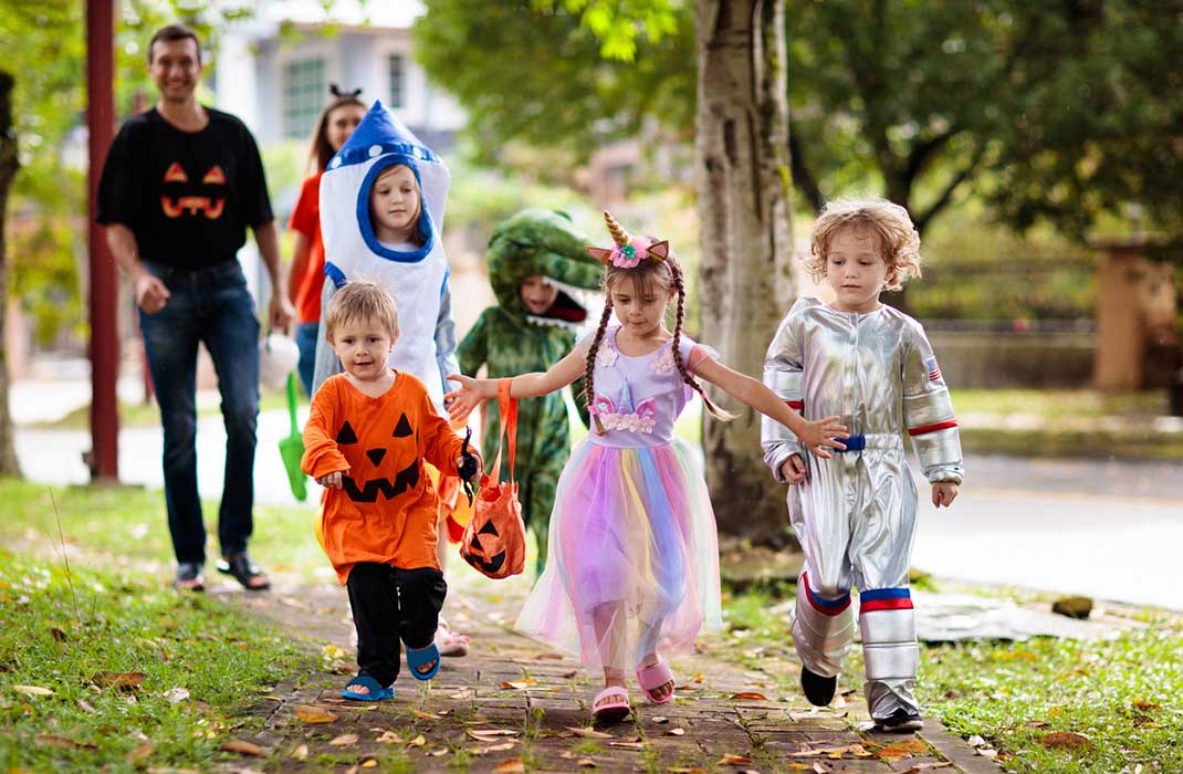 Costumed children trick-or-treating with their parents in the background.