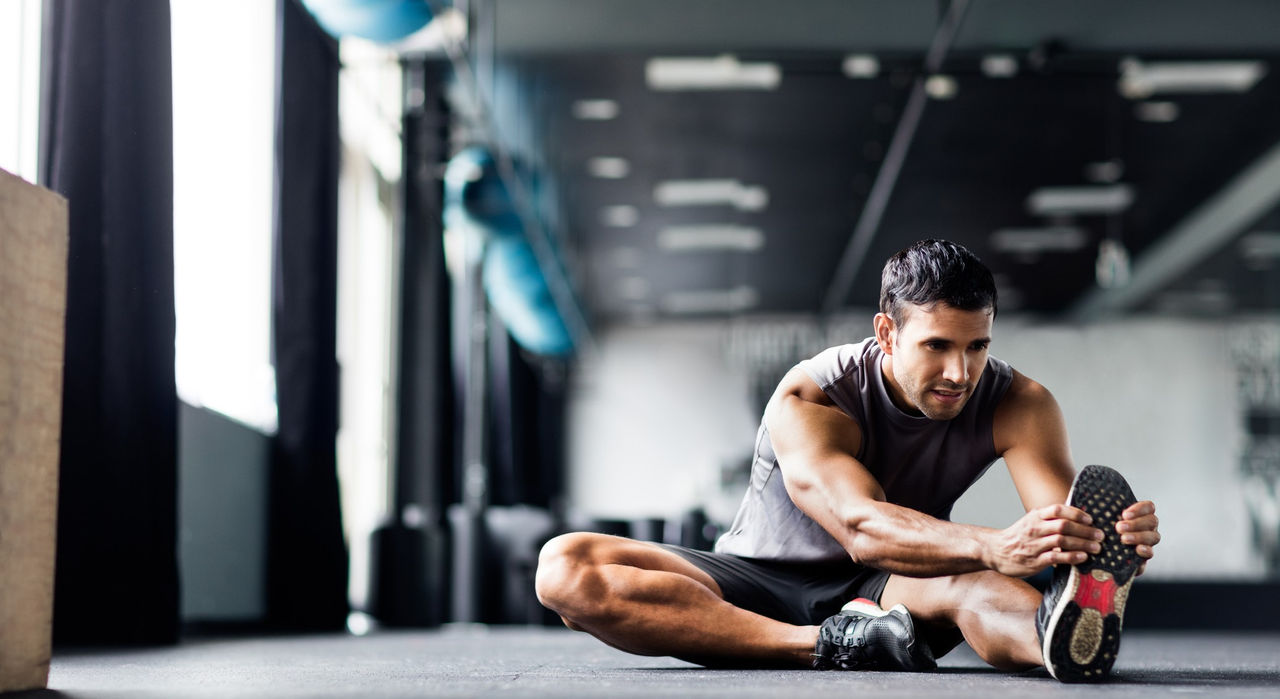 A male athlete does leg stretches in a gym.