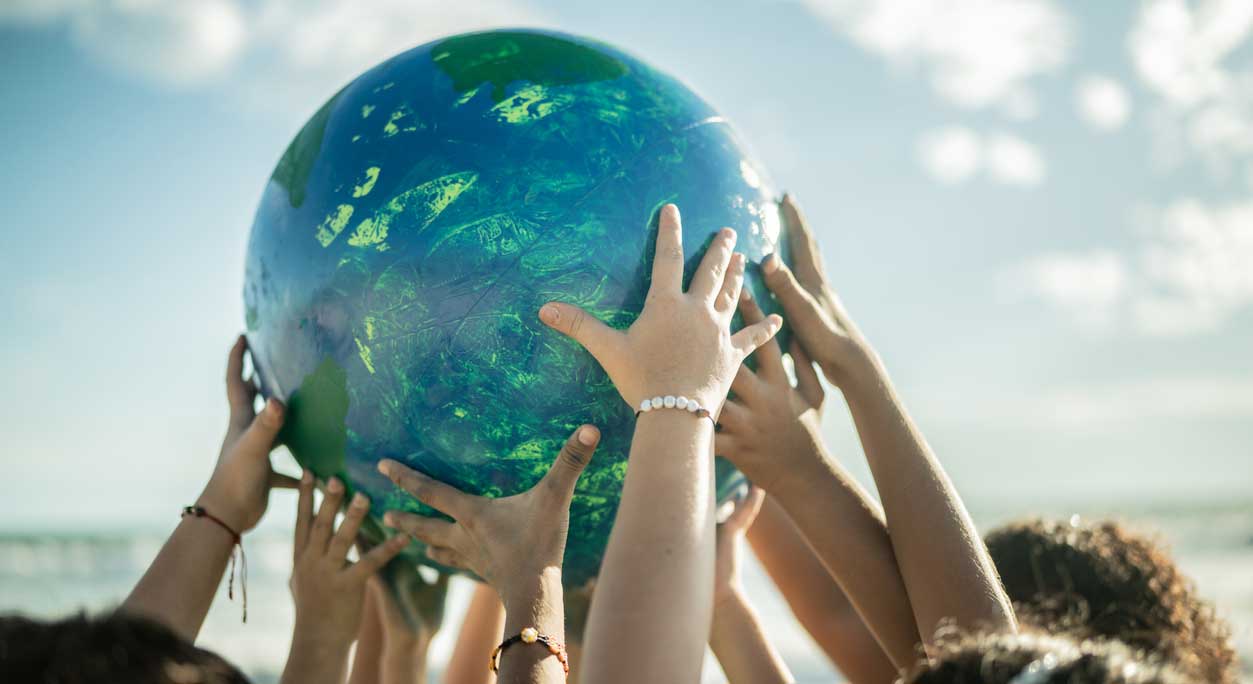 Many hands holding up a globe against a background of sea and sky.