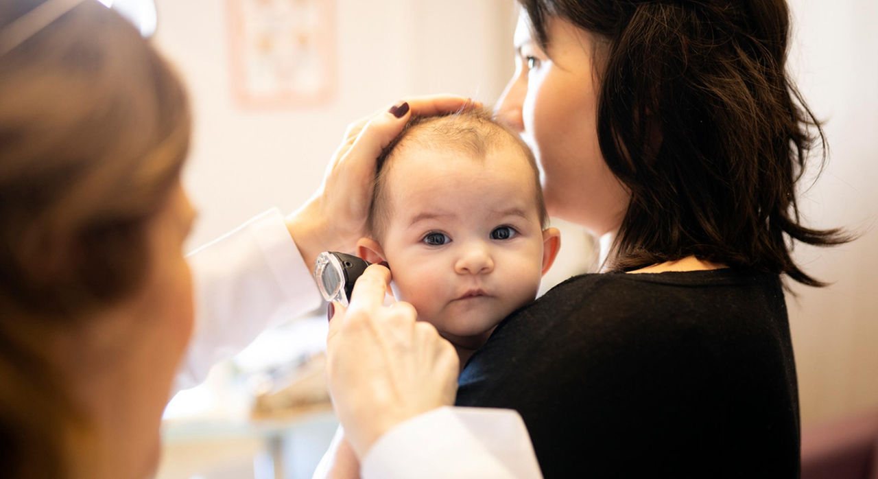 Doctor checking a baby carried by their parent for hearing loss