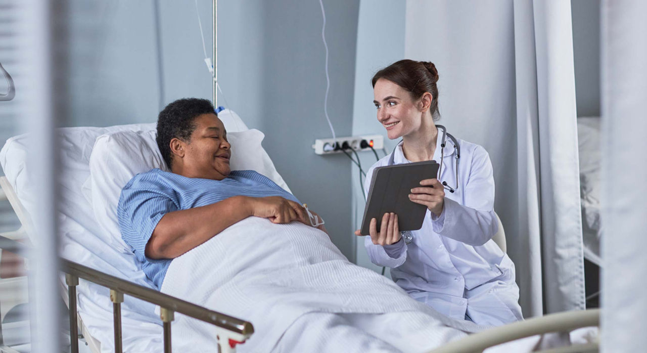 A patient in a hospital bed talks with their doctor