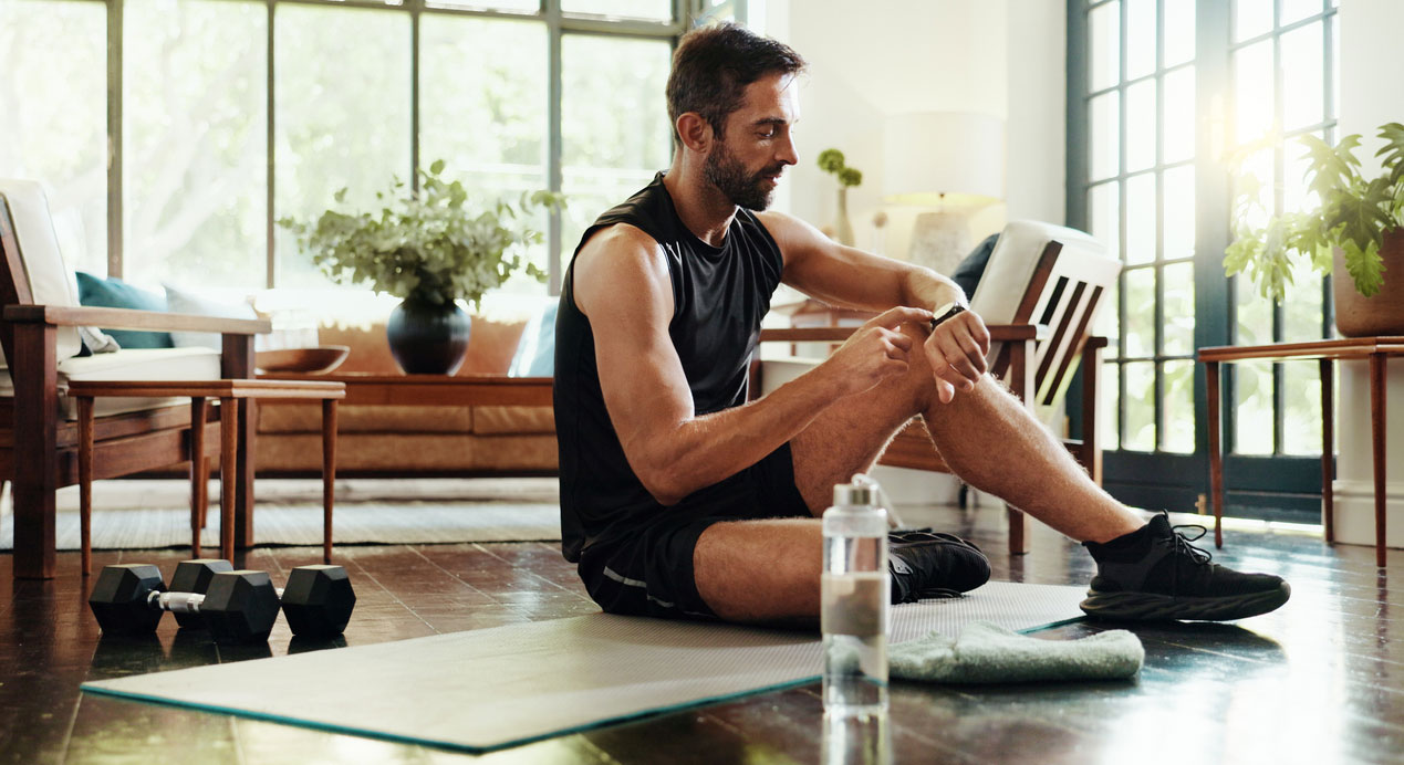 An early 30s white man checking his heart rate zone while working out in his living room.