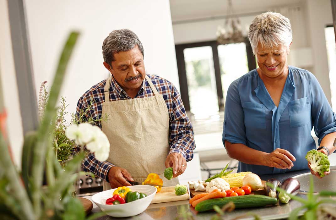 An older couple chops colorful vegetables together.