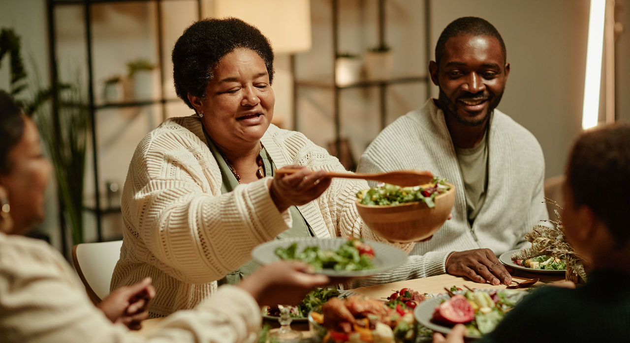 Portrait of smiling African-American grandmother serving food while celebrating Thanksgiving with big happy family at dinner table