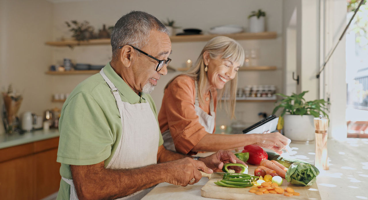 An older couple smiling while chopping vegetables for a healthy meal.