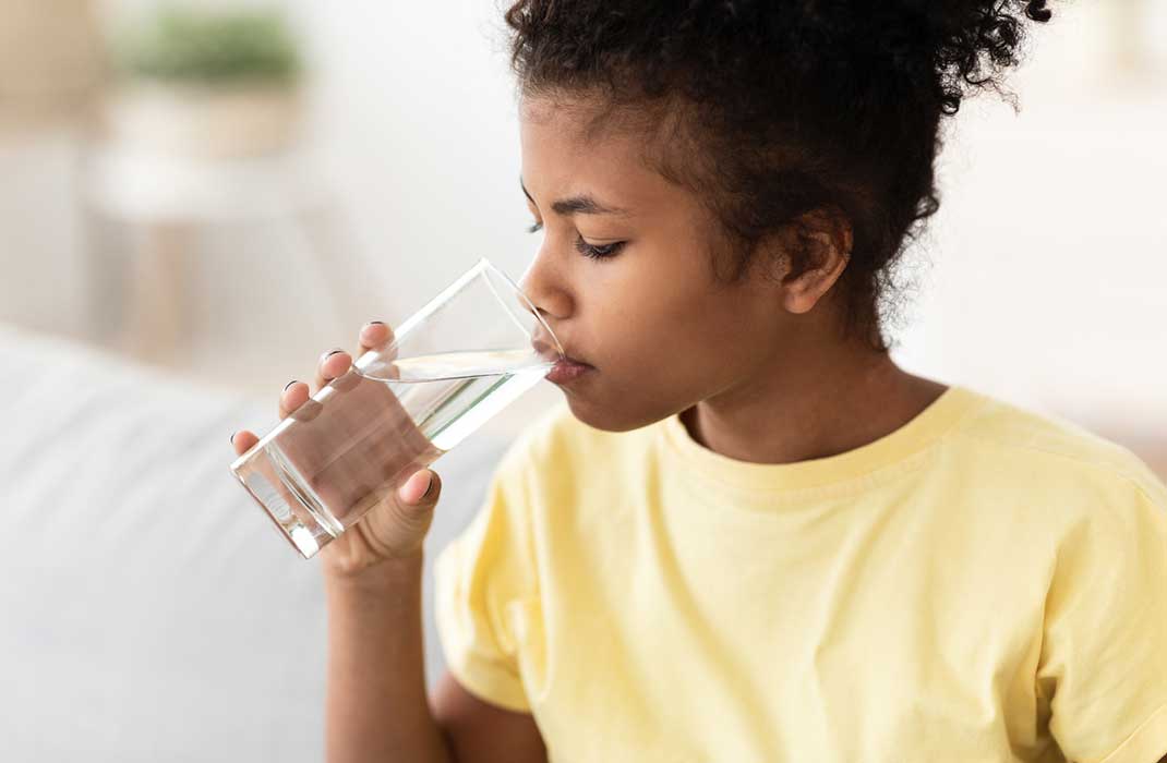 A little girl drinks a glass of water.