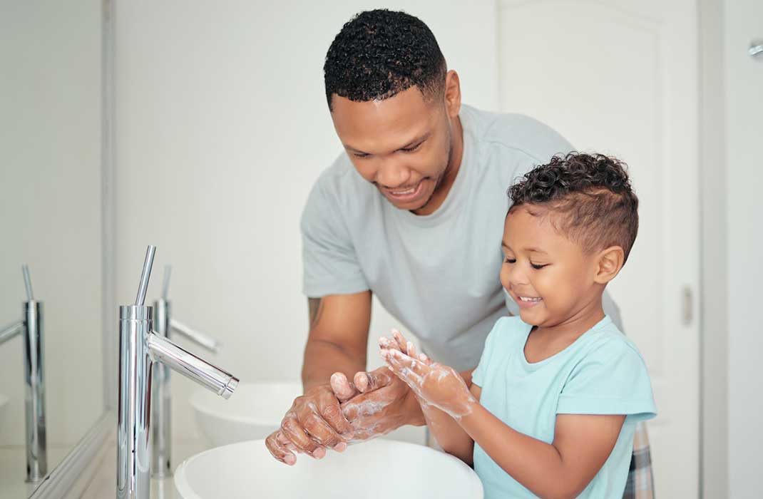 A father and his small son wash their hands together.