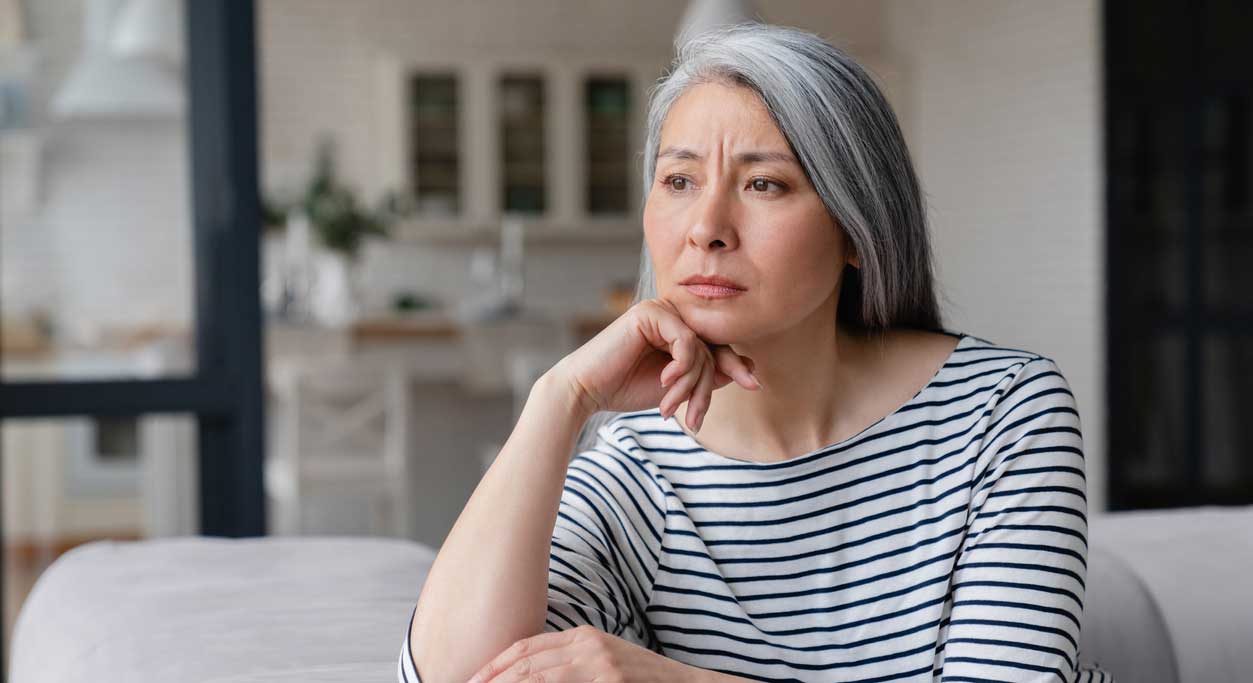 A worried older woman looks out her living-room window.