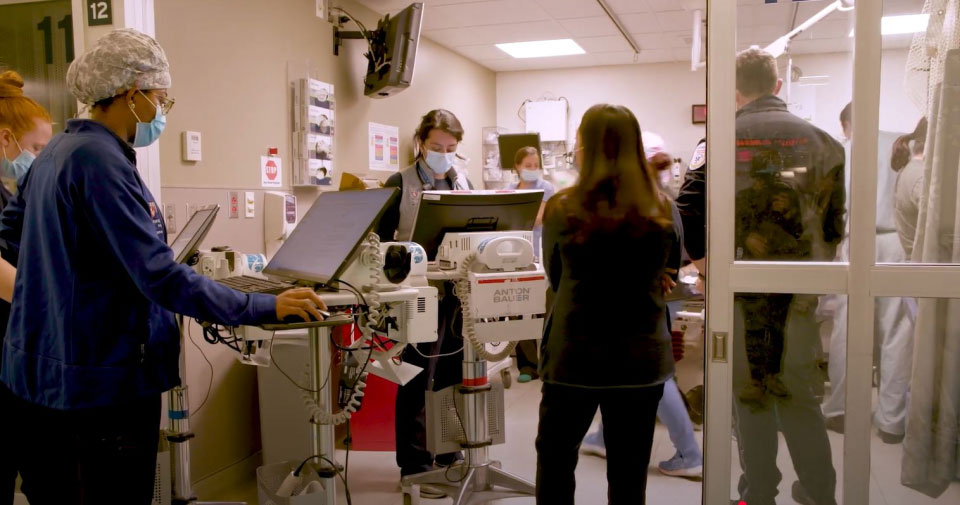 Practitioners, students, and a police officer  conferring in a hospital hallway.