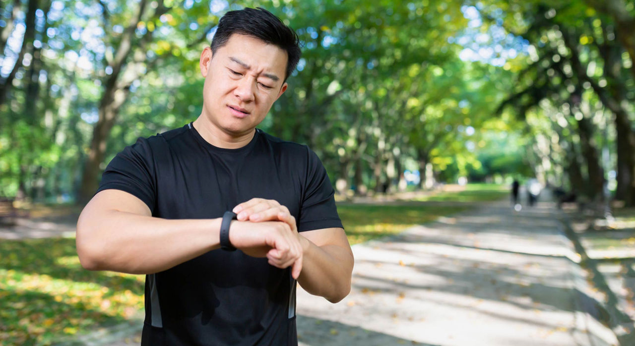 A man running in a park checks his smartwatch and looks concerned about an irregular heartbeat