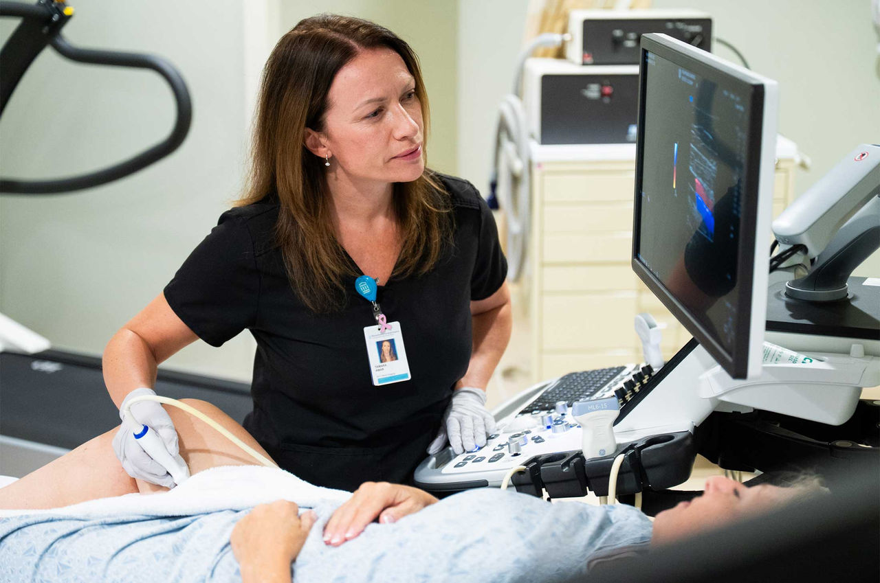 A health care provider conducts a vascular ultrasound exam for chronic limb-threatening ischemia, placing the wand on a patient's leg and checking the screen.