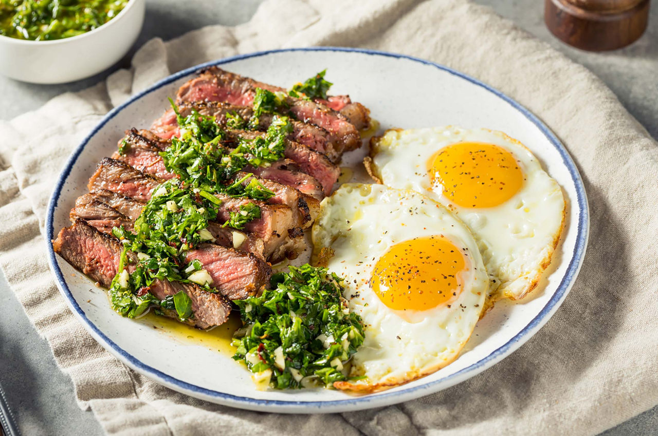 Steak and eggs on a white plate garnished with greens and black pepper