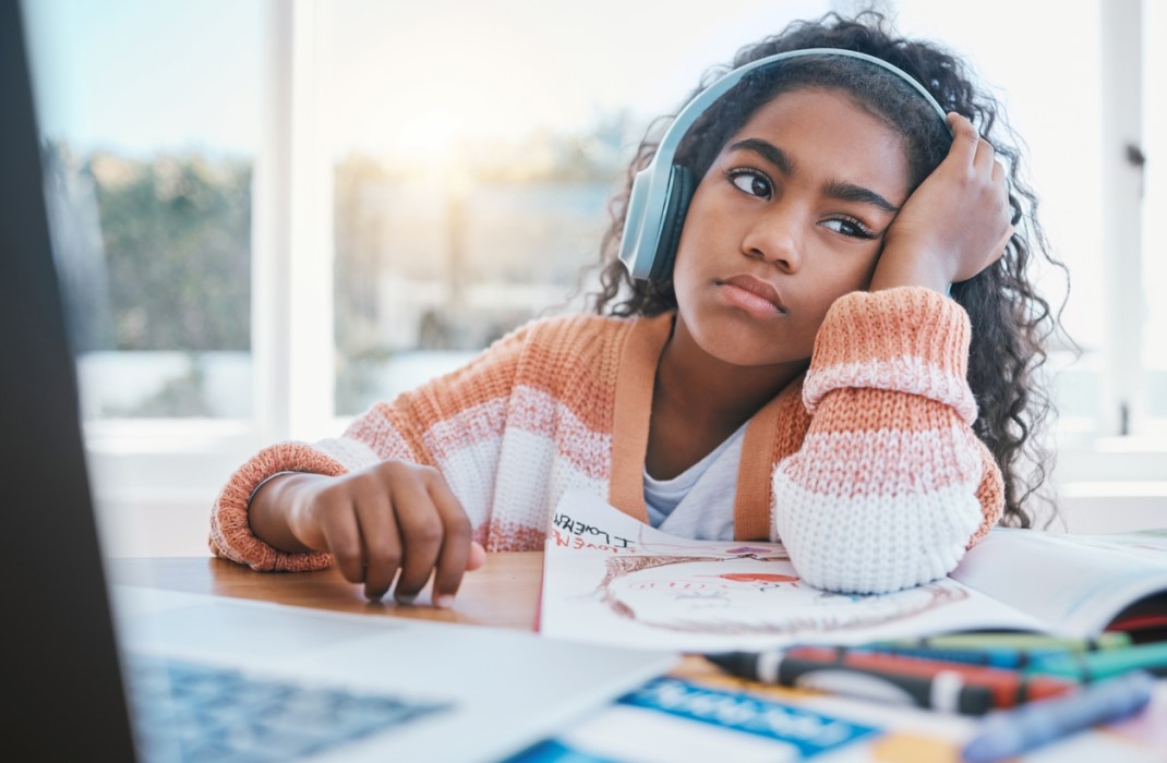 Young girl with headphones on appearing distracted and bored while studying.