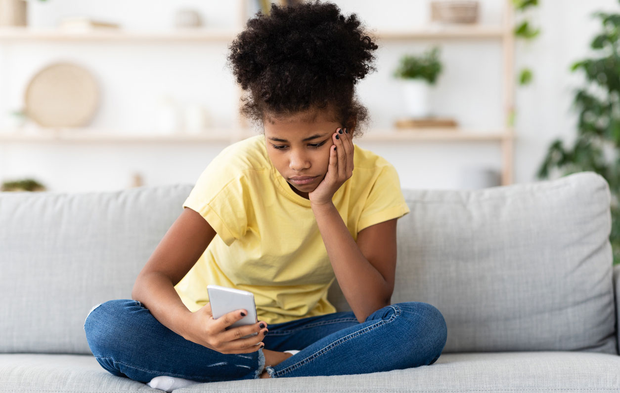 A sad-looking young girl reading something on her phone.