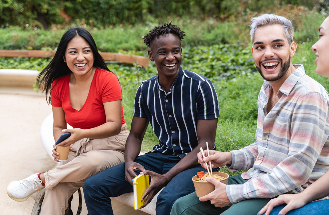 Four young people sitting outside and laughing together.