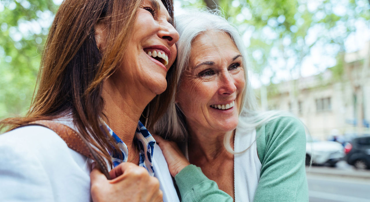 Two older women laughing and half-hugging each other on the street.