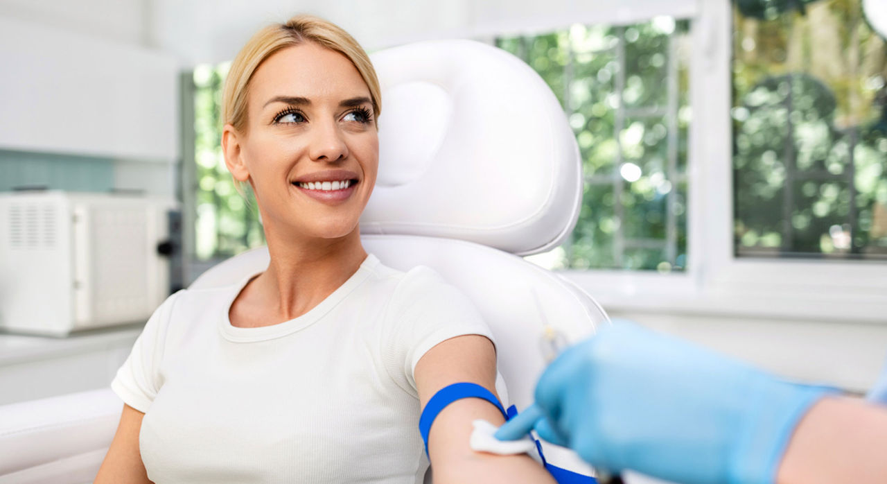 A provider’s gloved hand wipes the arm of a smiling woman to prepare for an Lp(a) blood test.
