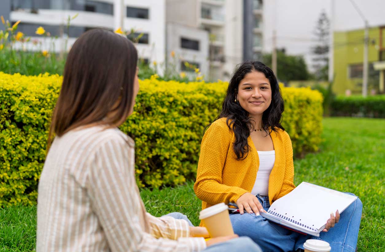 A young woman of color sitting outdoors and studying for college with a friend.