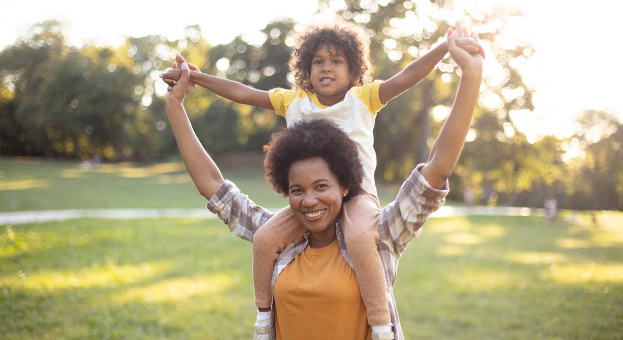 A child sits on their smiling mother's shoulders.