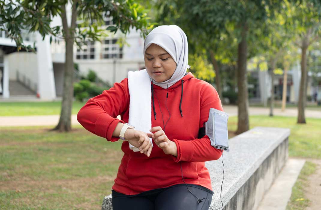 A walking woman consulting a watch-like device to monitor her heart rate.