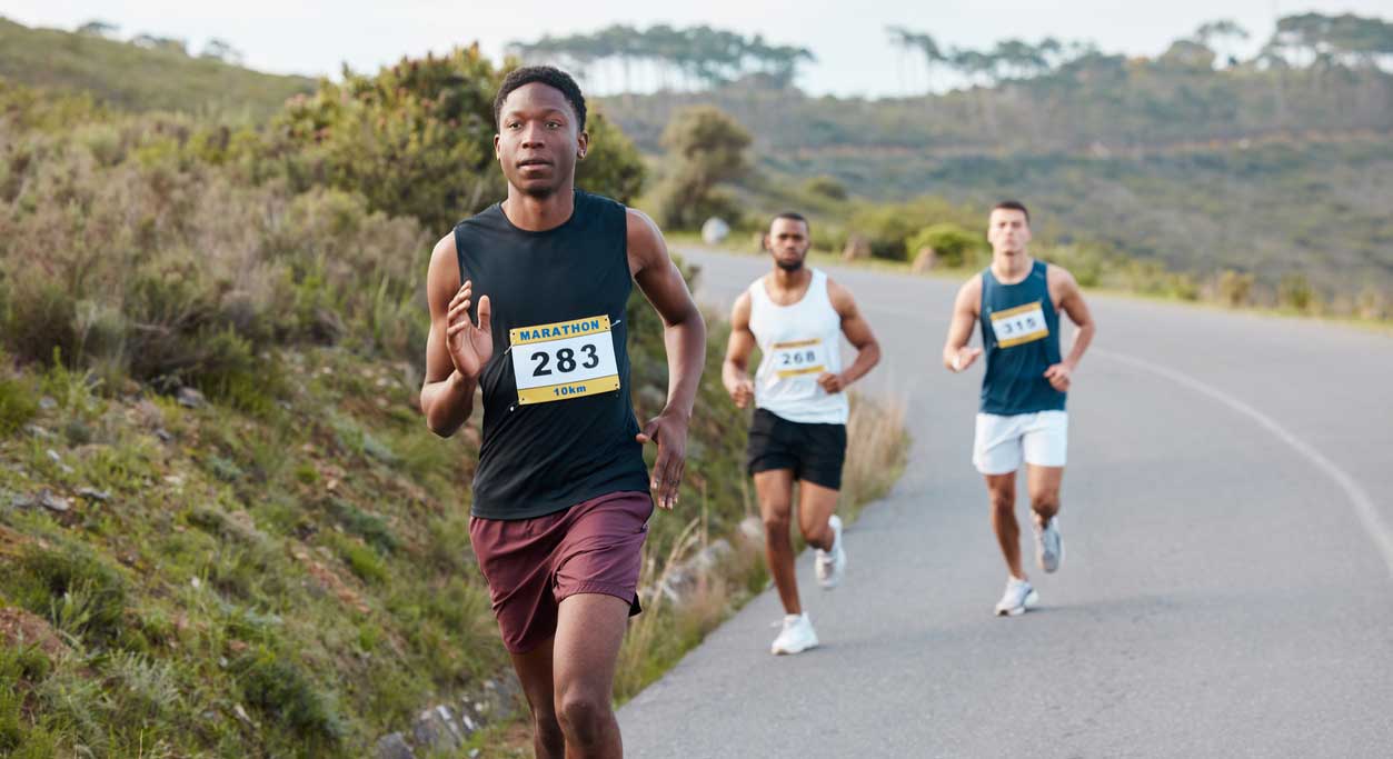 Three marathon runners coming around the bend of a country road.