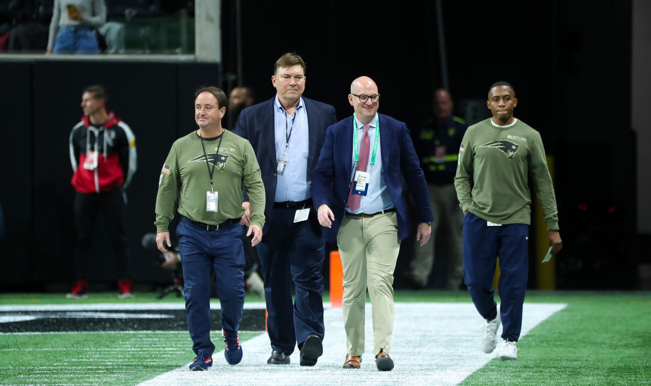 Four men, including Dr. Mark price, walk across the field during a Patriots game.