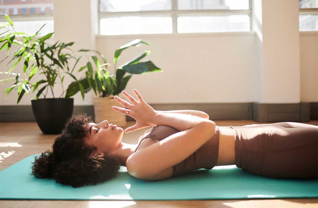 A woman meditating while lying on a yoga mat in her living room.