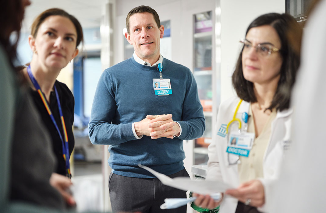 Eric Yenulevich, PA-C, participates in rounds on Braunwald Tower 11A, alongside Kate Martin, PA-C, and Denisa Gace, DO. The three are standing and look to be in discussion with a fourth person.