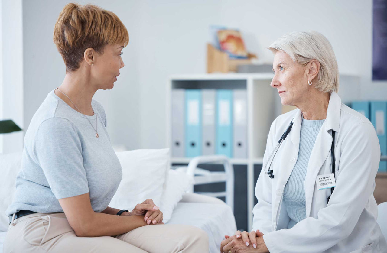 An older female doctor speaks with a concerned-looking middle-aged female patient.