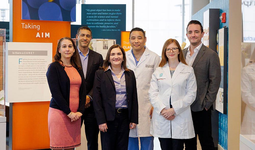 Six members of the INCIPIENT Team, two in lab coats, in front of a museum exhibit about cancer treatment.