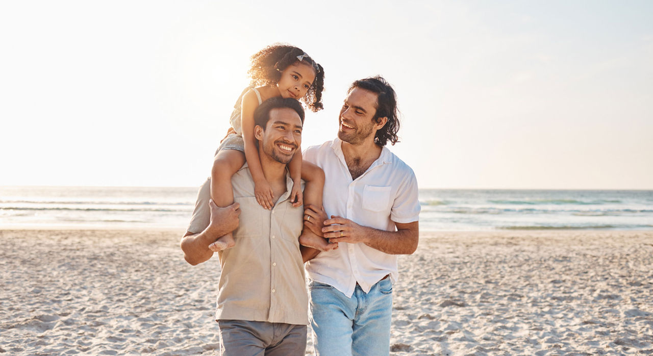 Family of two men and daughter walk on the beach