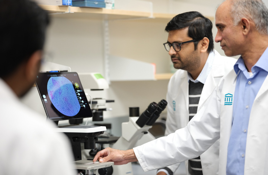 Three men in lab coats review the results of a scan on screen.