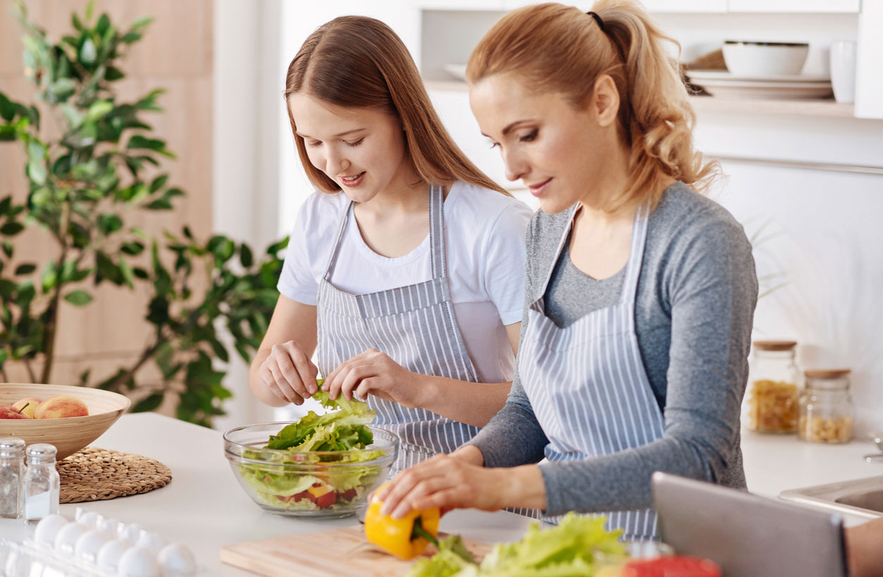 A mother and daughter prepare a salad in a bright kitchen.