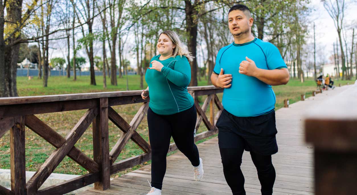 An overweight man and woman jogging in the park.