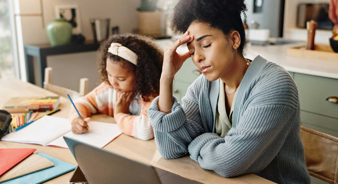 A tired mother helps her daughter with homework.