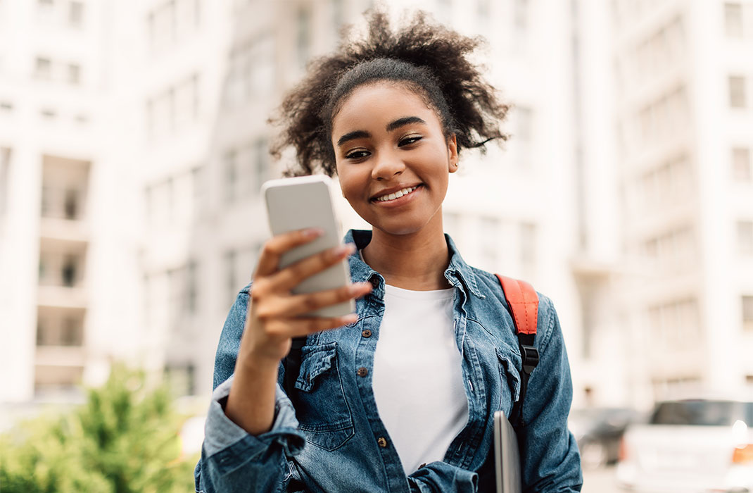 A young woman stands on a city street, checking her phone.