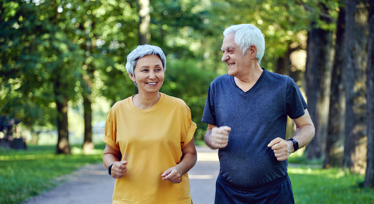 A happy older couple jogs lightly in the park.