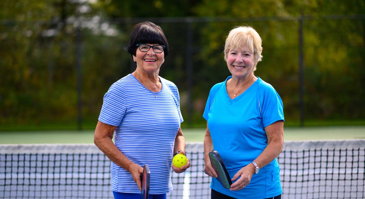Two older women posing on the pickleball court.