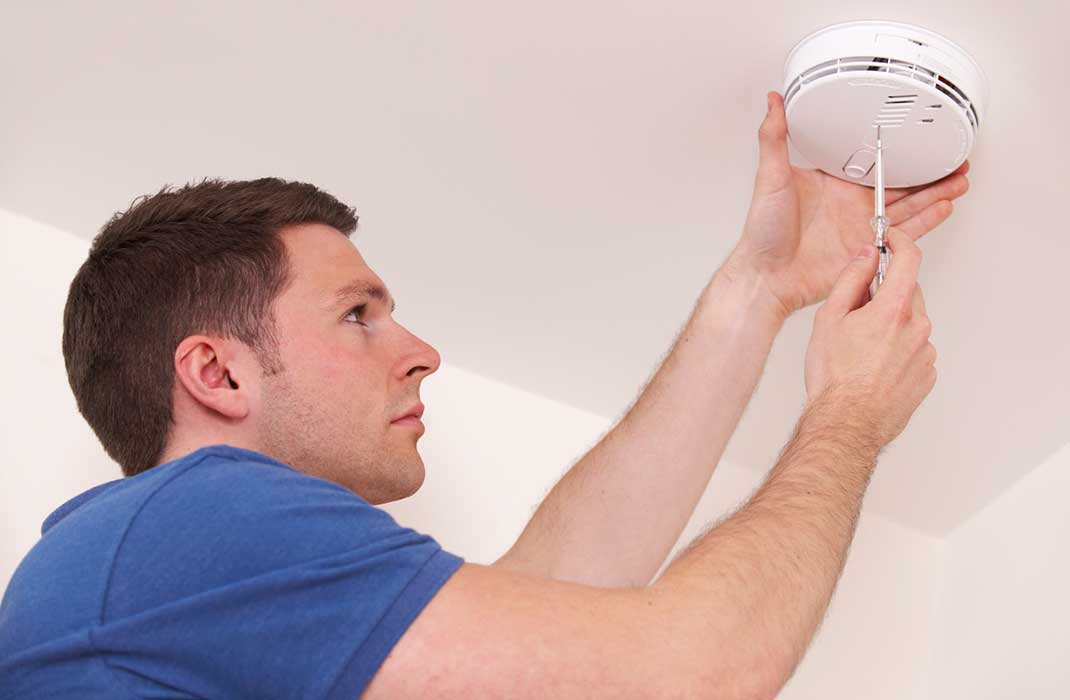 Man changes the battery of a carbon monoxide detector.